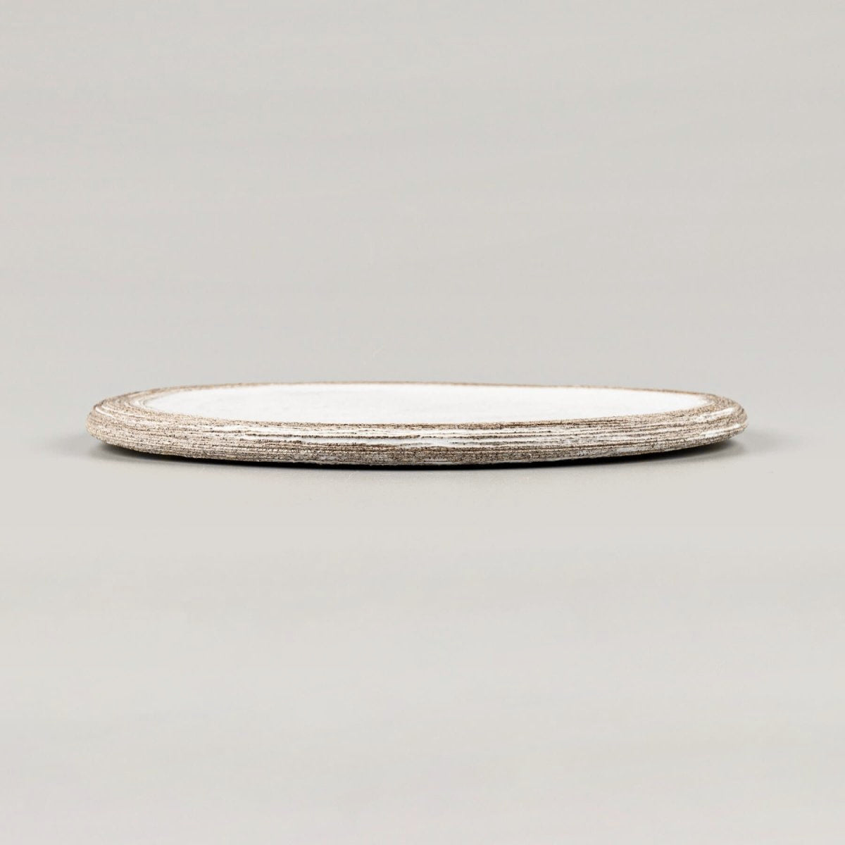 Side view of a luxury handmade ceramic plate in matte white finish over dark clay.