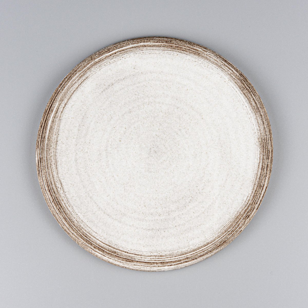 Flat handmade ceramic plate with carved rims and matte white glaze for fine dining presentation.