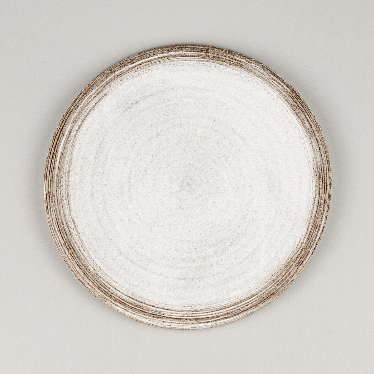 Flat handmade ceramic plate with carved rims and matte white glaze for fine dining presentation.