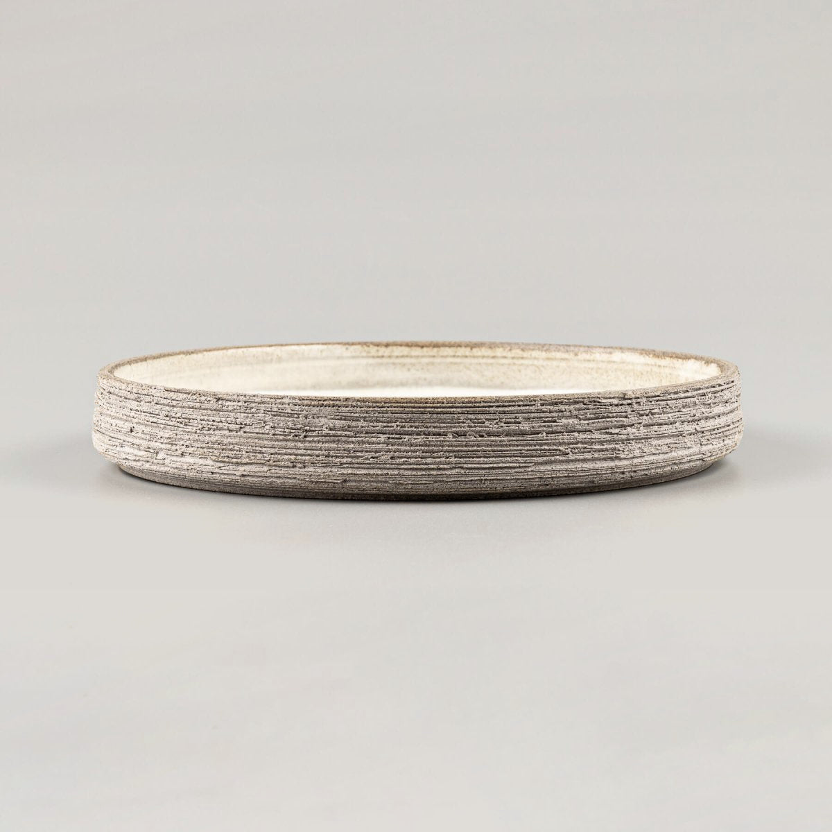 Handmade stoneware plate with raw textured exterior and smooth glazed interior.