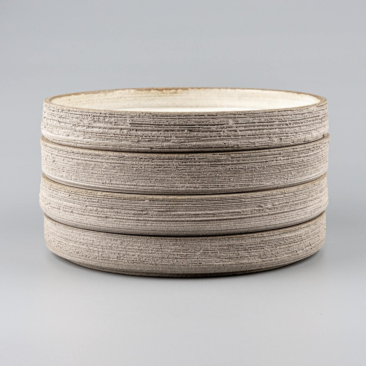 Stack of handcrafted stoneware dinner plates with raw textured sides and smooth glazed tops.