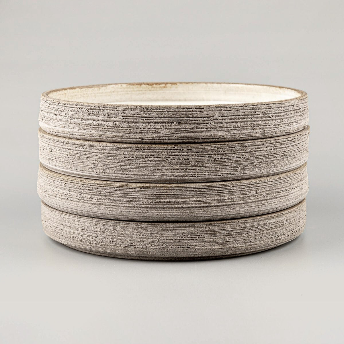 Stack of handcrafted stoneware dinner plates with raw textured sides and smooth glazed tops.
