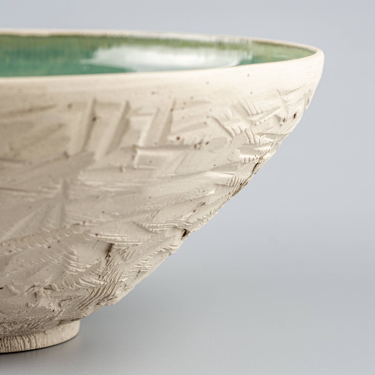 Detail of unglazed ceramic surface showing rough hand-carved pattern on serving bowl.