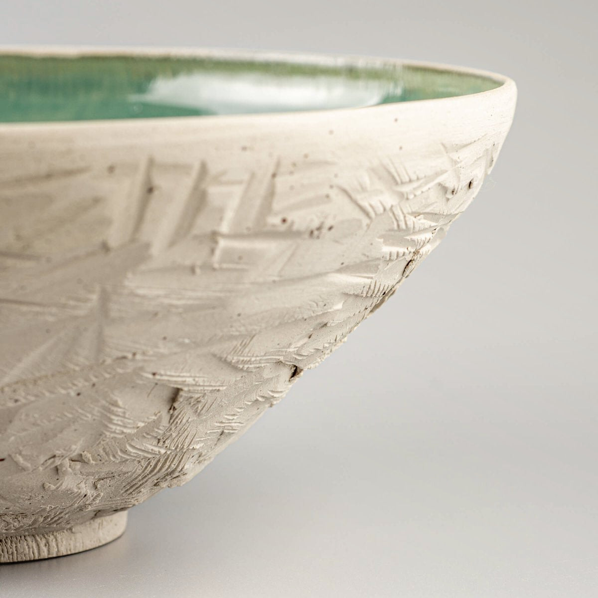 Detail of unglazed ceramic surface showing rough hand-carved pattern on serving bowl.