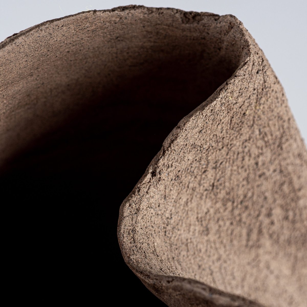Detail of a textured stoneware vase rim, showcasing an organic, handmade structure for luxury interiors.