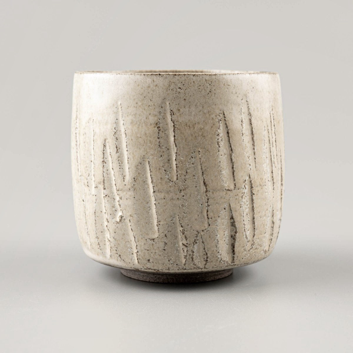 Side view of a ceramic handmade cup with textured carvings and artisanal glaze.