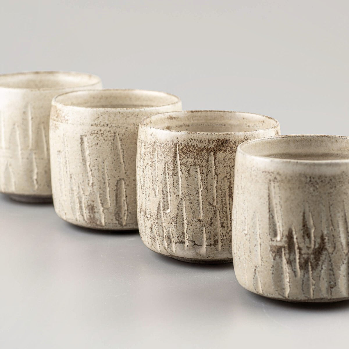 Four ceramic handmade cups aligned with matte finish and carved stoneware texture.