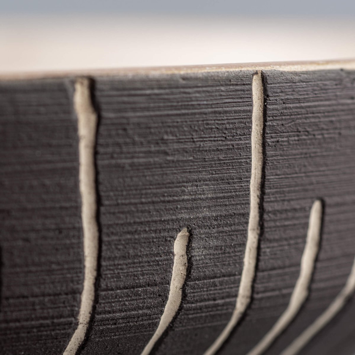Vertical grooves close-up carved into dark slip exterior of decorative ceramic bowl.