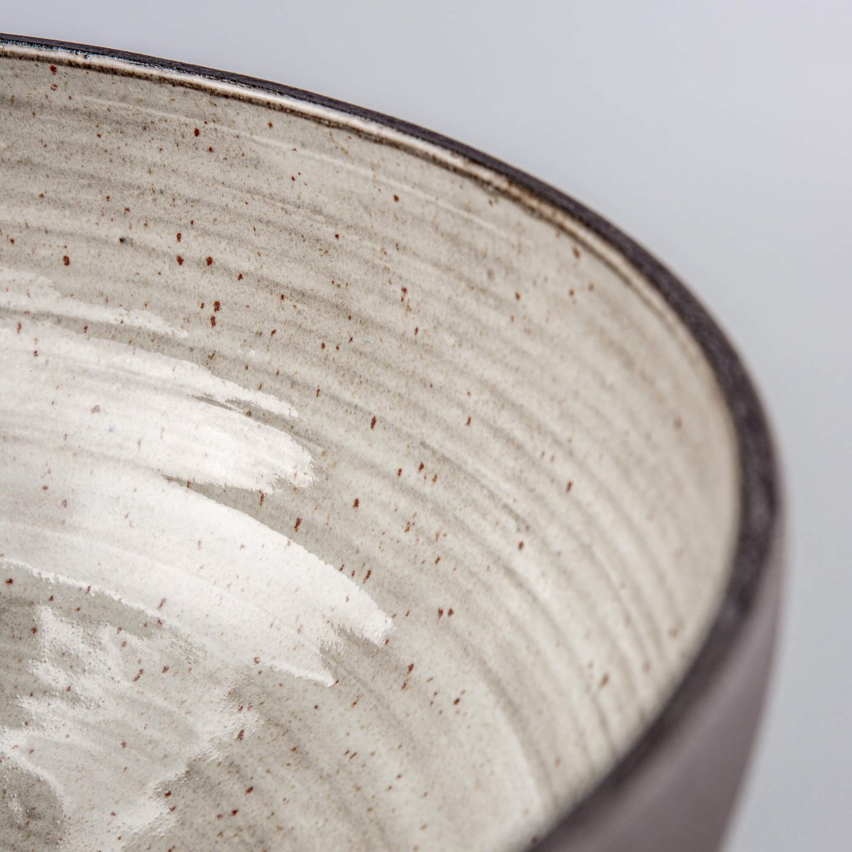 Detail of handmade serving bowl interior with speckled glaze, soft grey tones, and restaurant tableware texture.