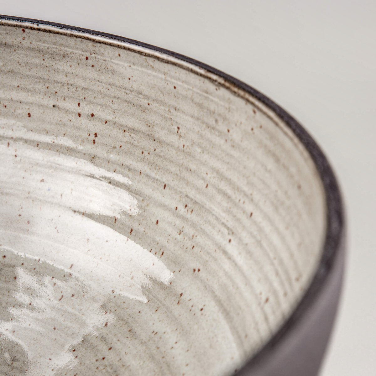Detail of handmade serving bowl interior with speckled glaze, soft grey tones, and restaurant tableware texture.