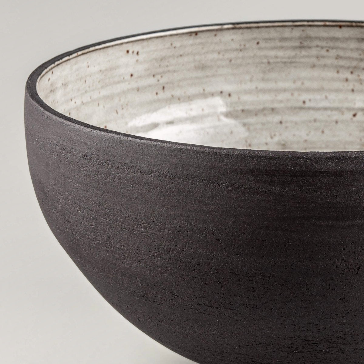 Close-up of handmade serving bowl with glossy cream glaze, dark rim, and speckled handmade ceramic detail.
