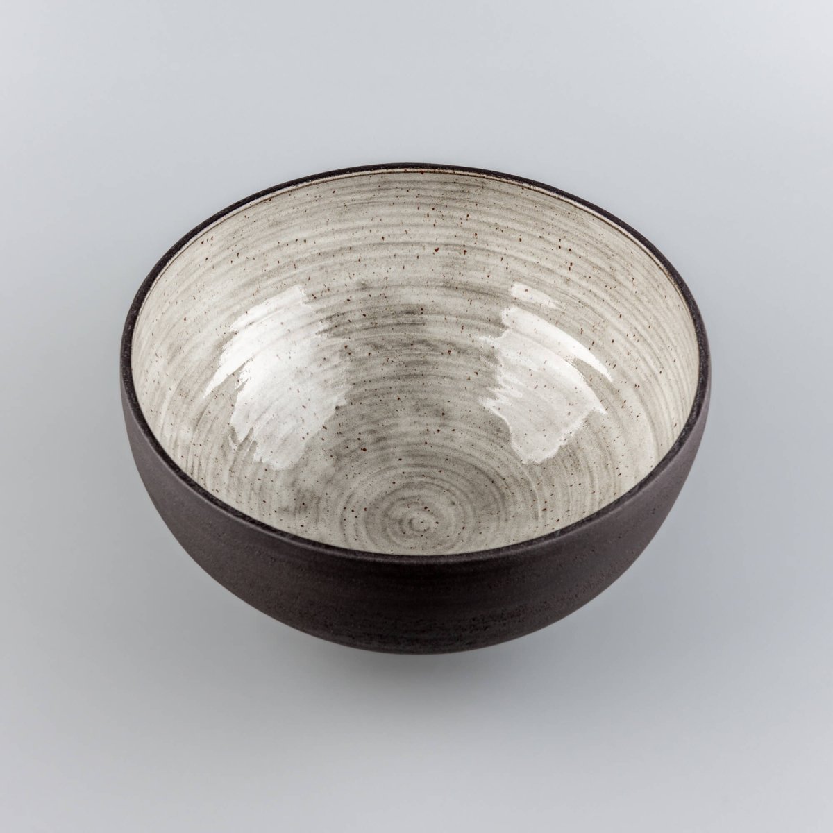 Top view of handmade serving bowl with light speckled interior, dark rim, and handmade pottery texture.