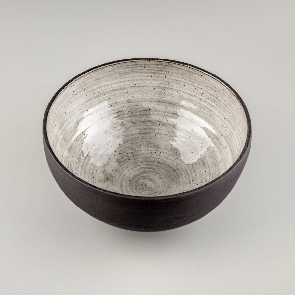 Top view of handmade serving bowl with light speckled interior, dark rim, and handmade pottery texture.