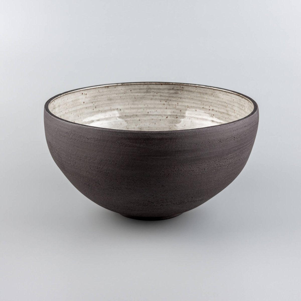 Handmade serving bowl with dark textured exterior and light speckled glaze, ideal centerpiece or fruit bowl.