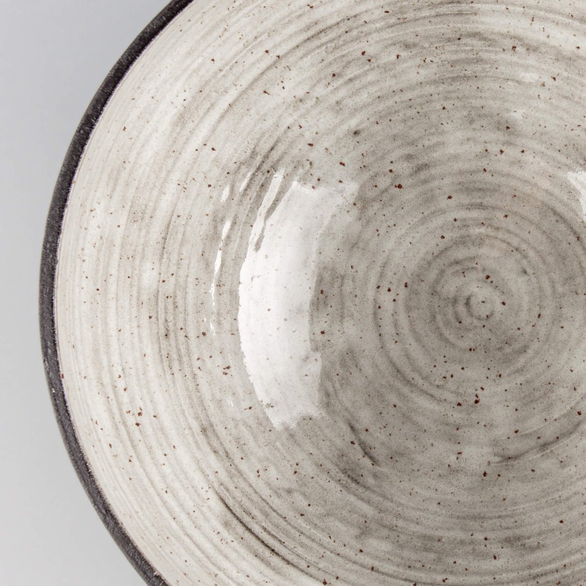 Angled close-up of handmade serving bowl with dark rim, cream glaze, and boutique hotel tableware style.