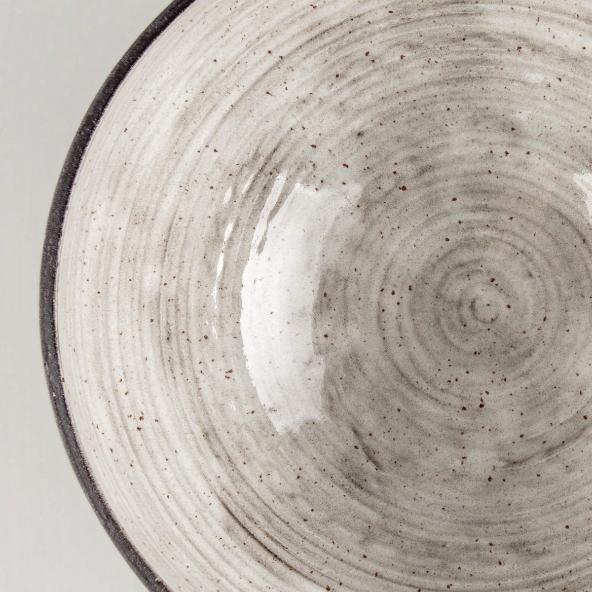Angled close-up of handmade serving bowl with dark rim, cream glaze, and boutique hotel tableware style.