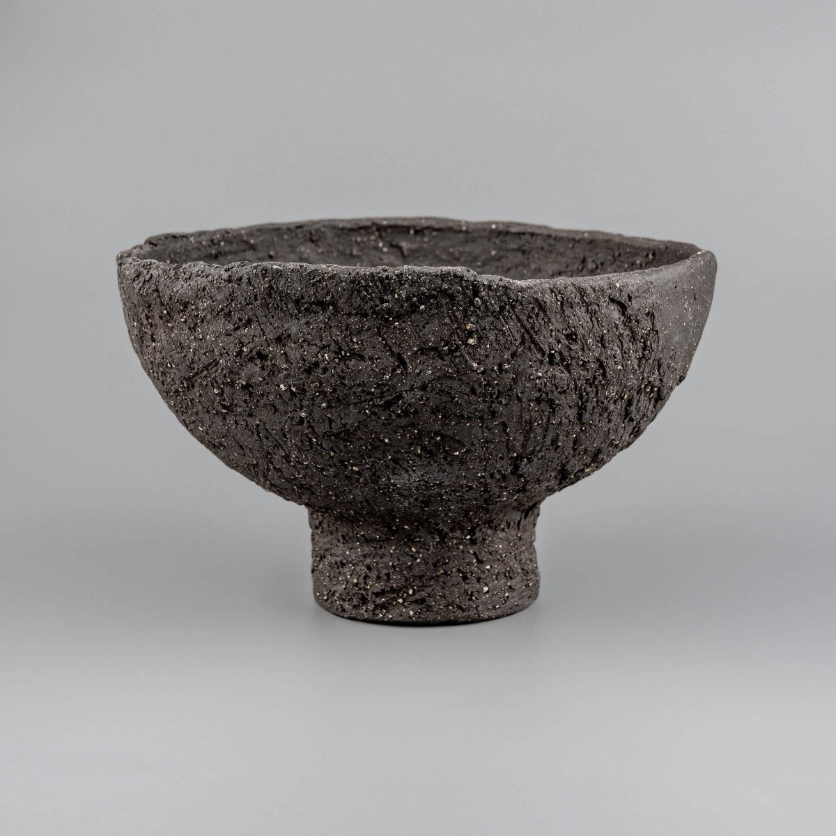 Handmade decorative bowl with rough black ceramic texture, elevated foot, and sculptural form for boutique hotel decor.