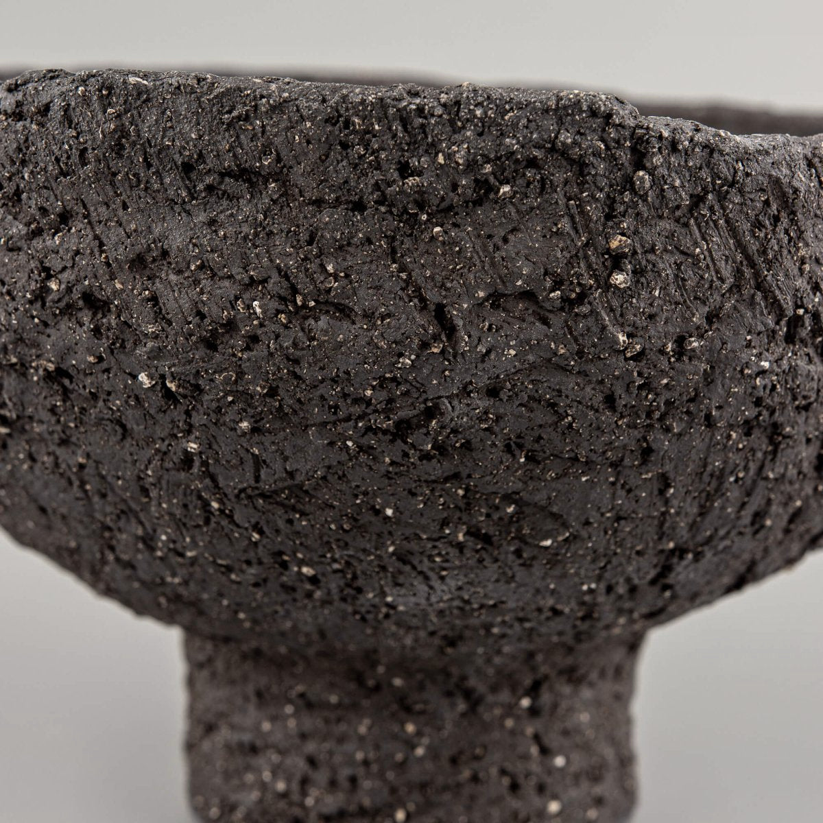 Side detail of handmade decorative bowl with organic rim, dark stoneware texture, and boutique hotel interior appeal.