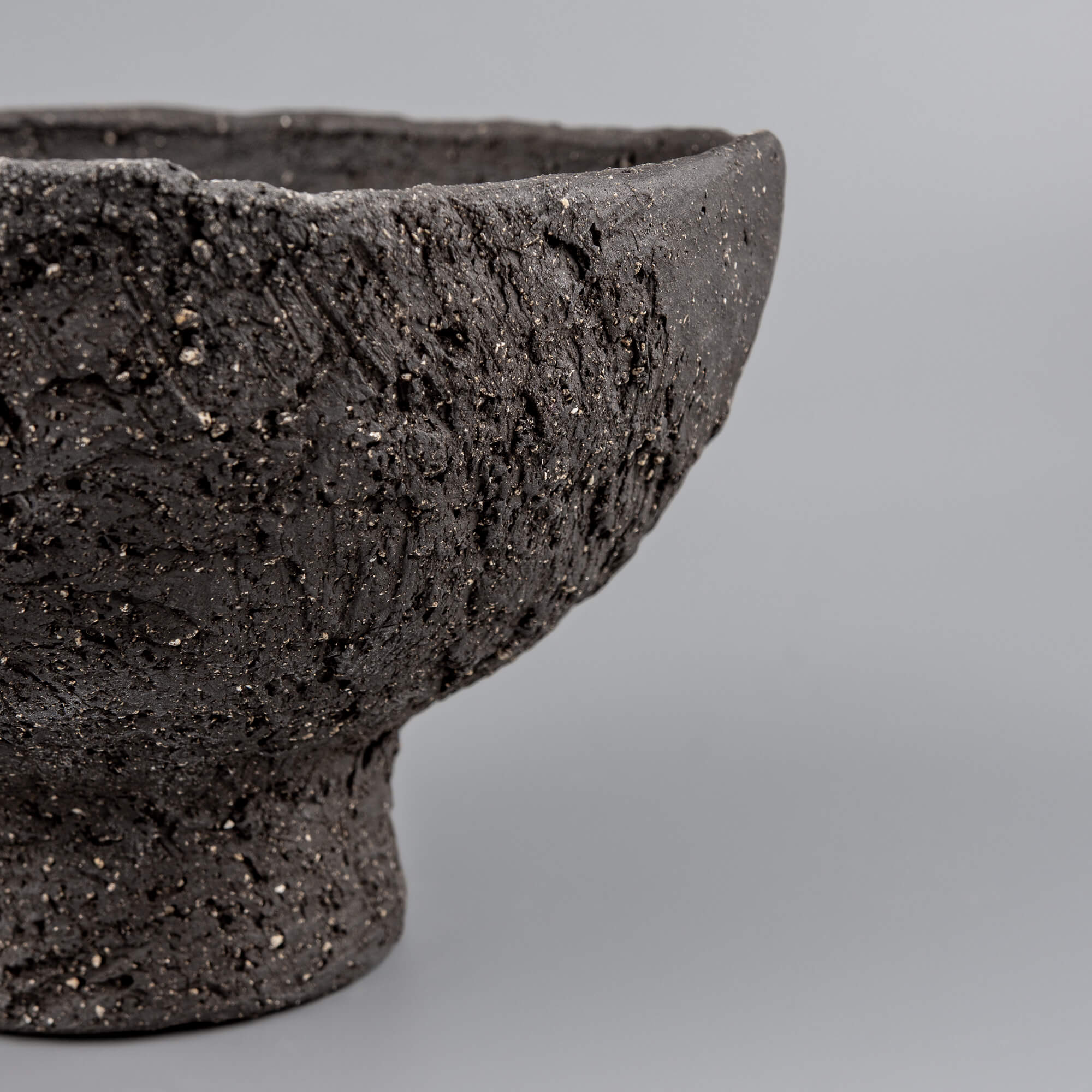 Macro view of handmade decorative bowl texture with raw black clay, carved marks, and collectible pottery character.