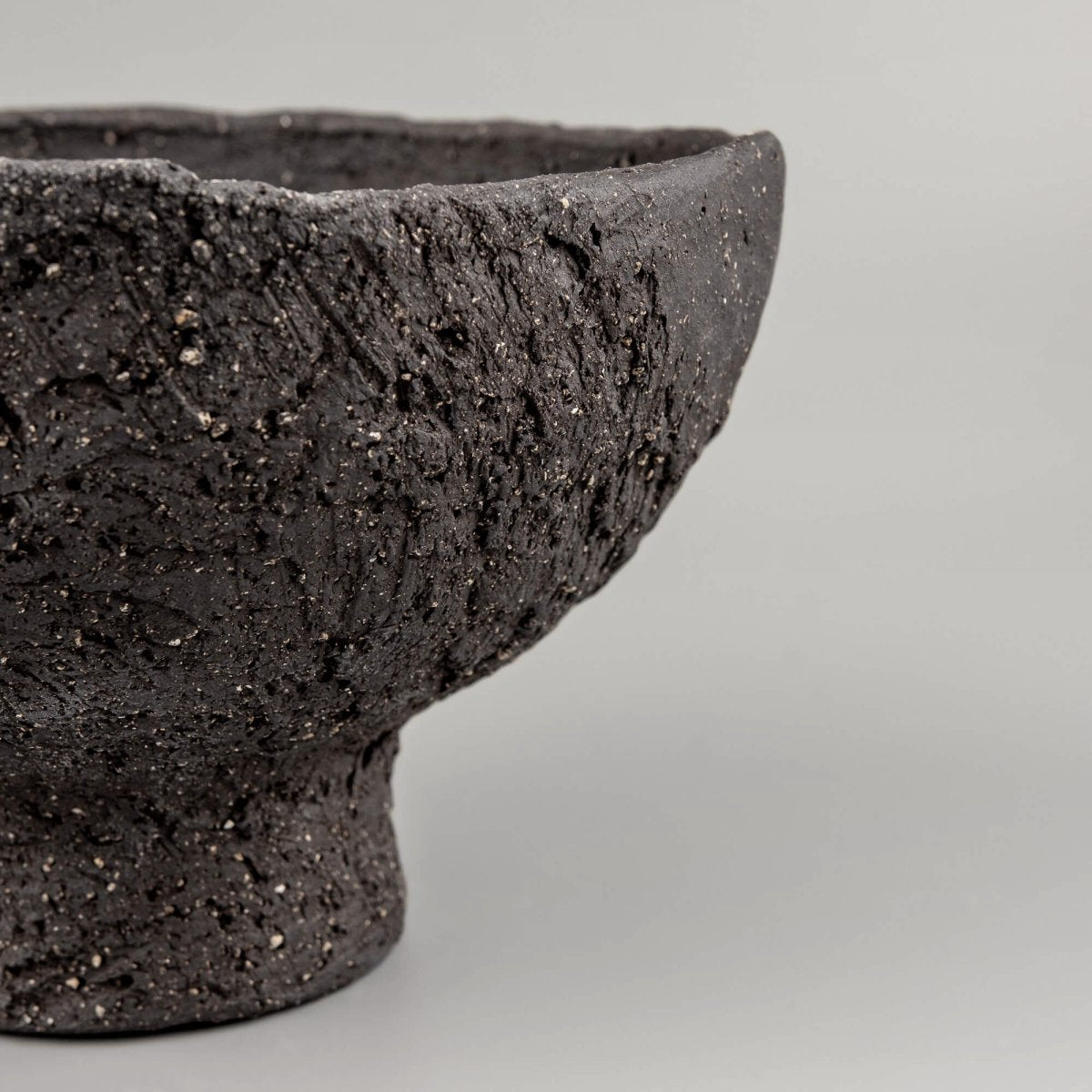 Macro view of handmade decorative bowl texture with raw black clay, carved marks, and collectible pottery character.