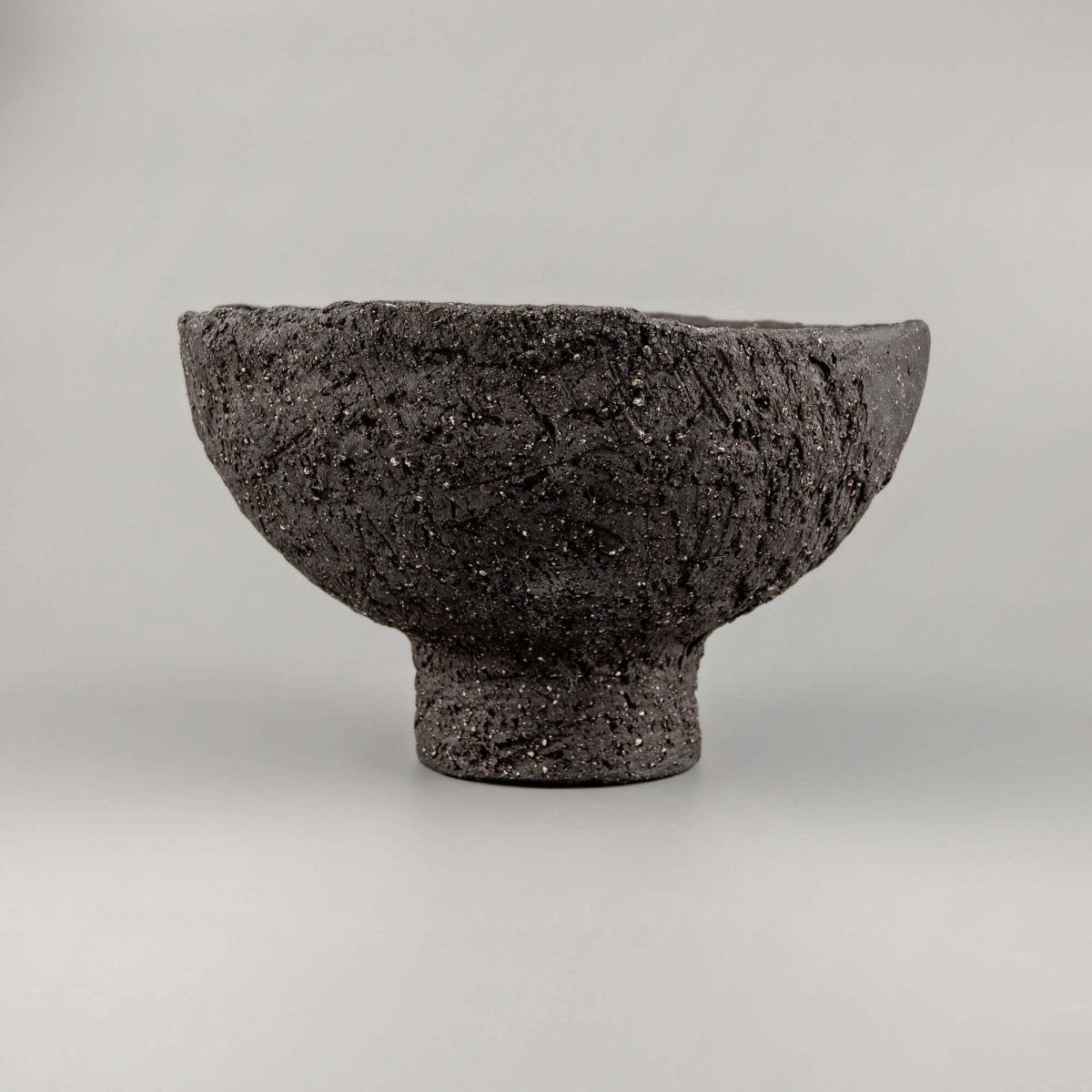 Textured handmade decorative bowl with black clay surface, pedestal base, and bold presence for home or hotel interiors.