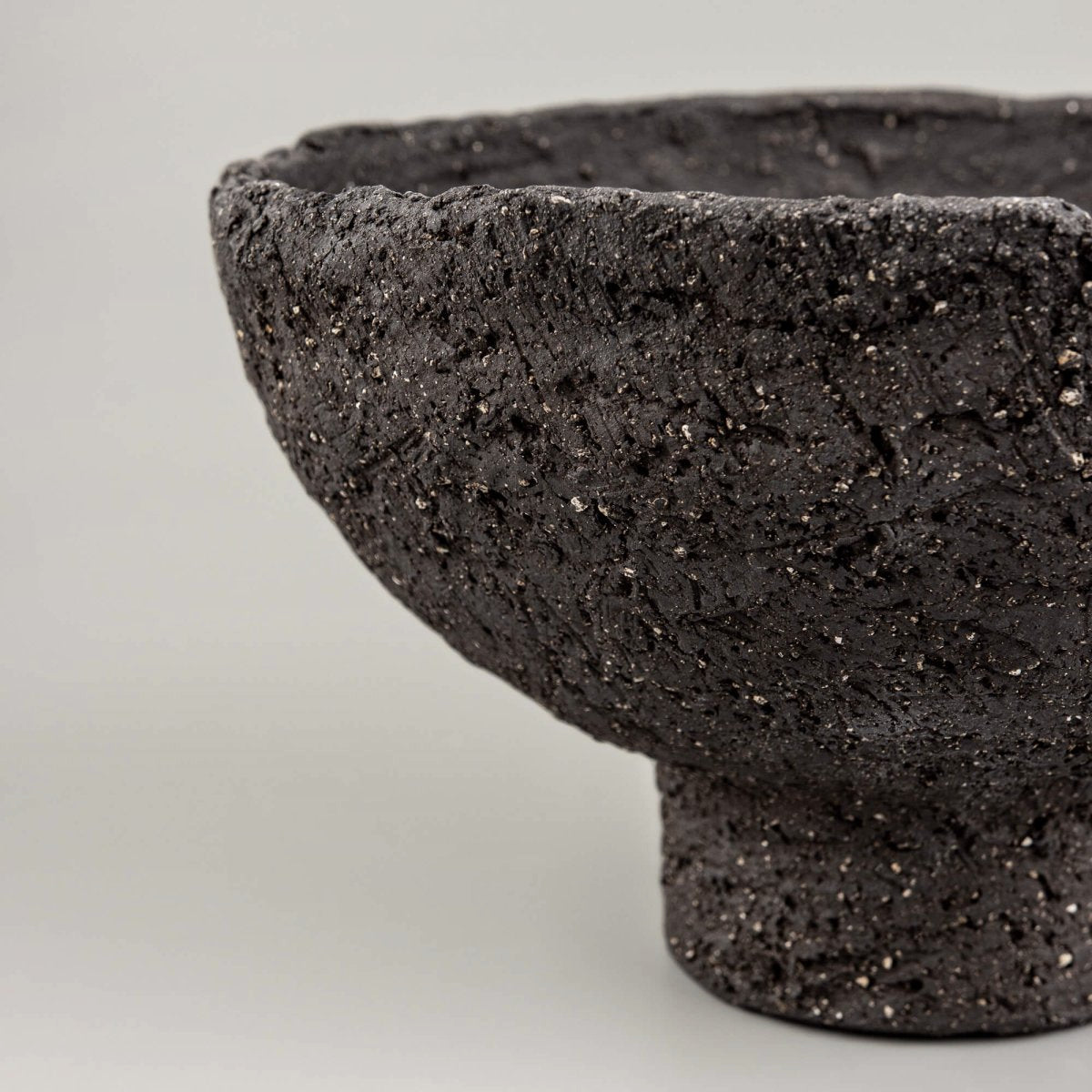 Close-up of handmade decorative bowl with rough black ceramic surface, mineral speckles, and artisan texture detail.