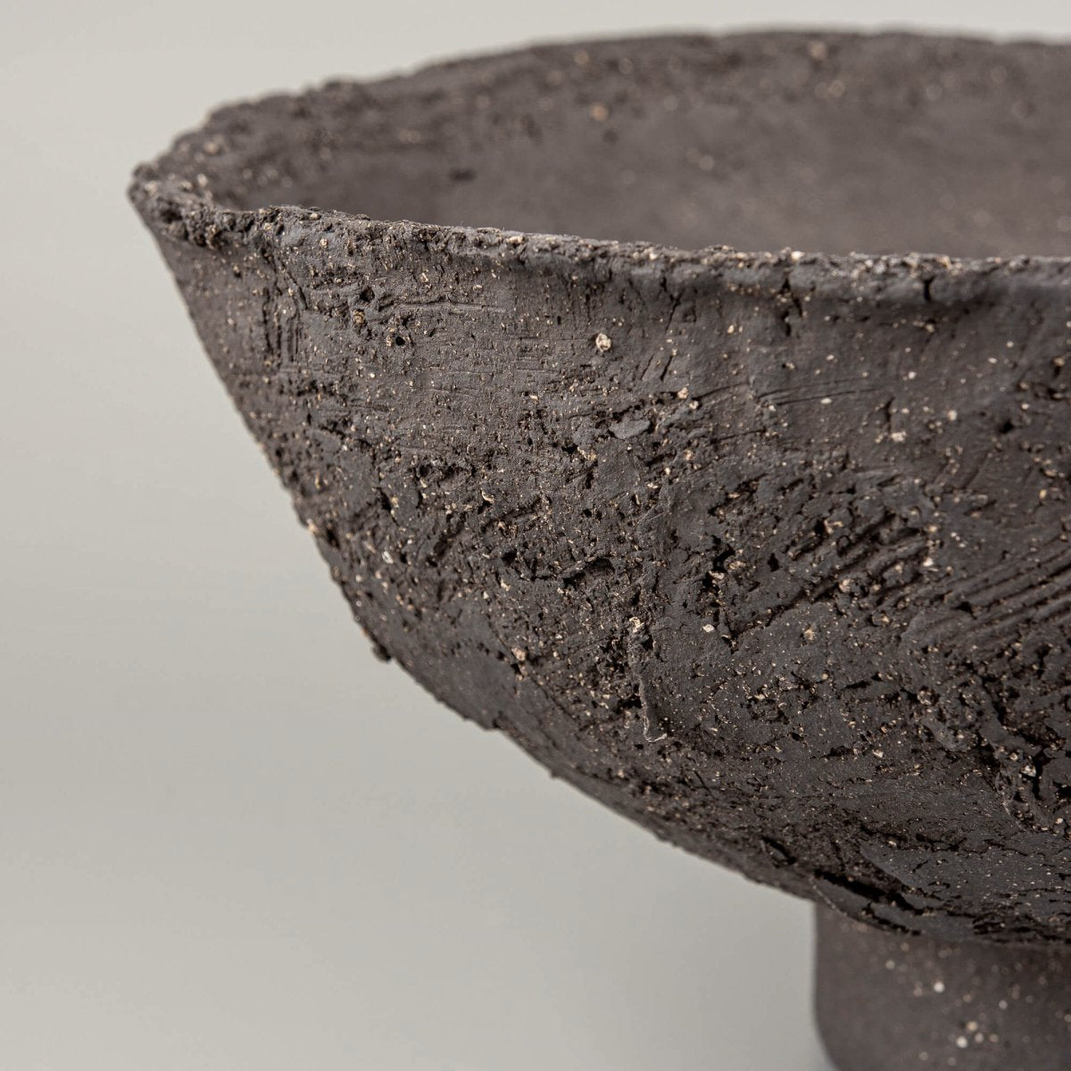 Handmade decorative bowl close-up showing rough stoneware texture, mineral speckles, and artisan ceramic surface.