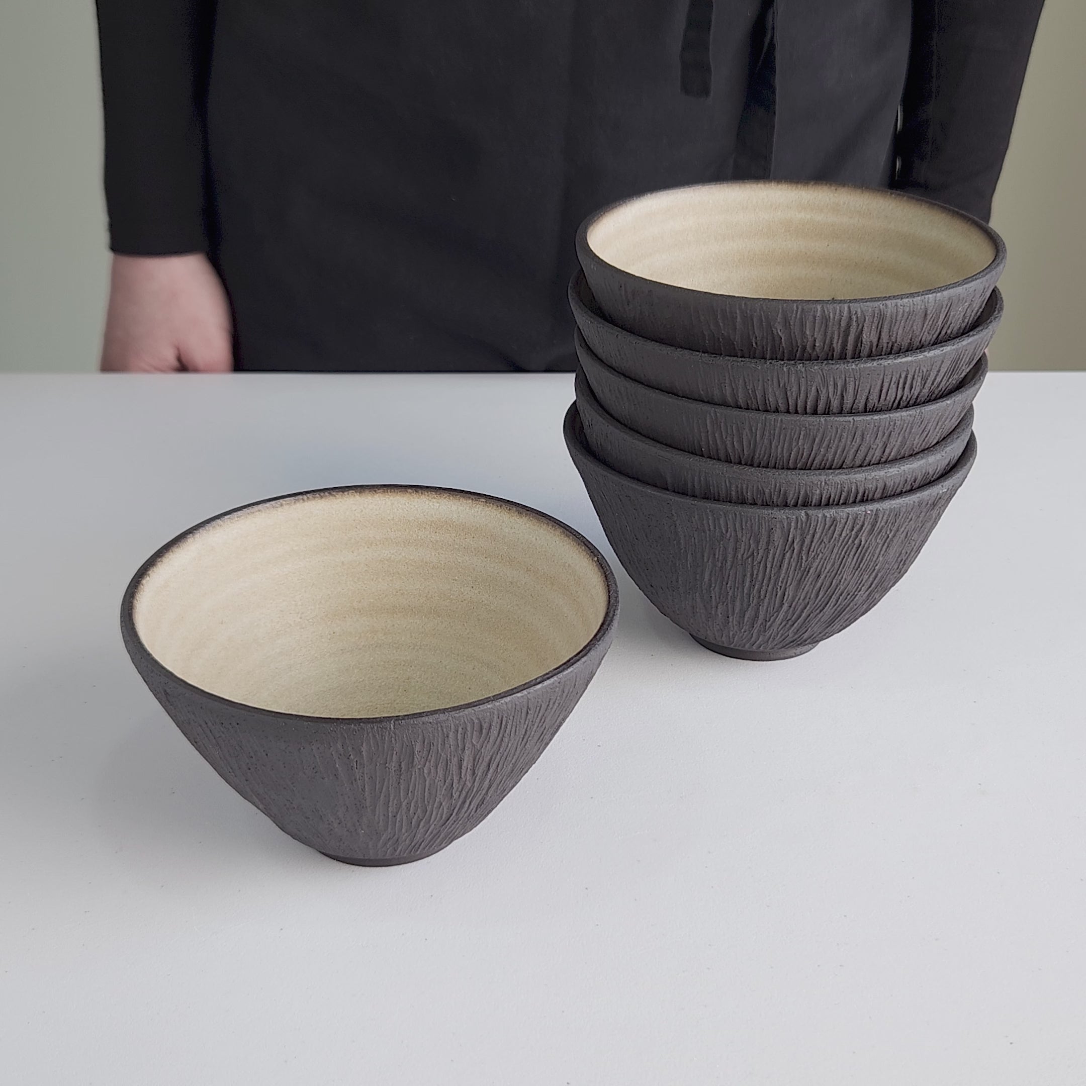 Elegant video showcasing a rotating handmade stoneware bowl, designed with raw textured black clay and smooth beige interior, perfect as collectible tableware for luxury restaurants, boutique hotels, or refined home dining settings.