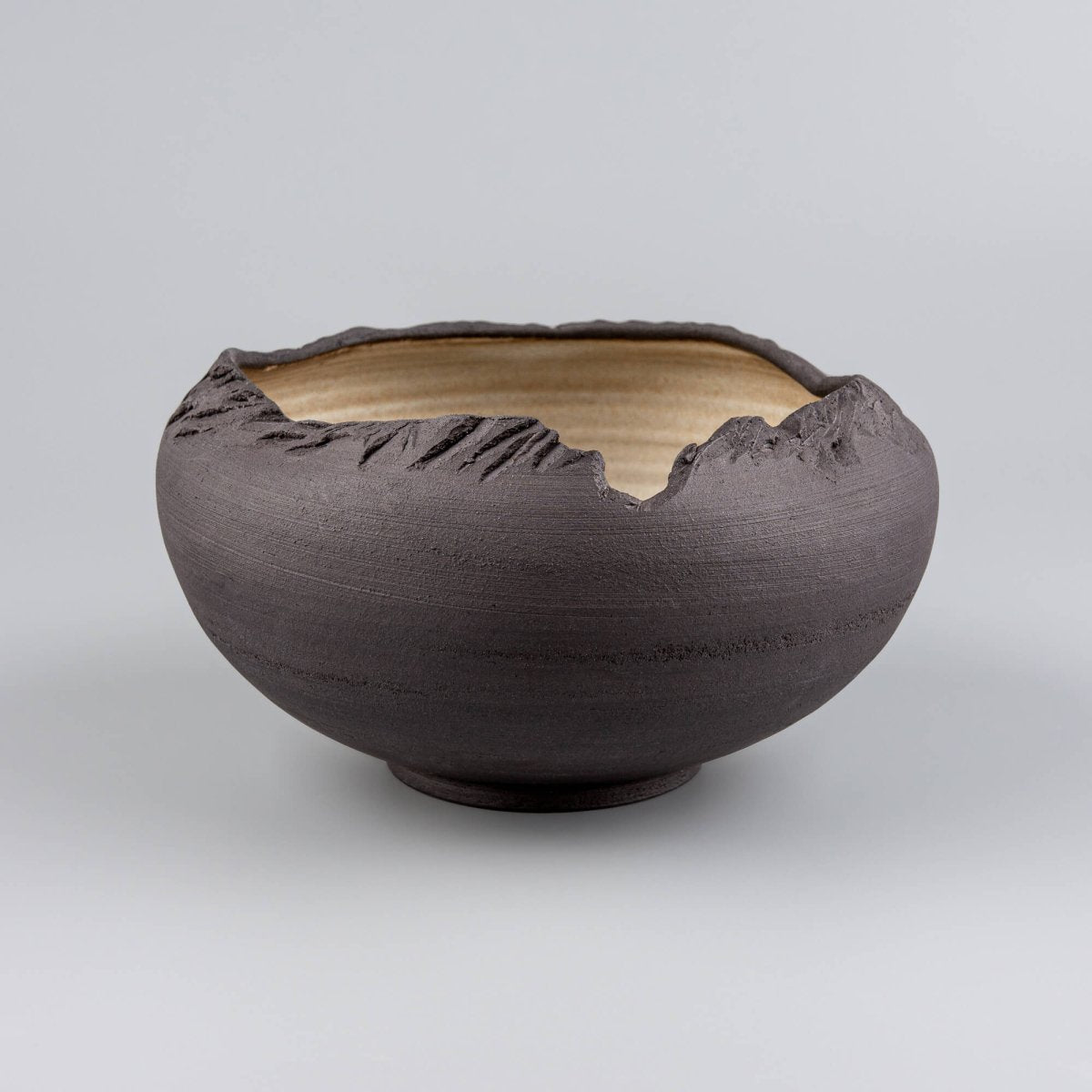 Side view of handmade stoneware bowl with carved raw black exterior and sculptural open rim.