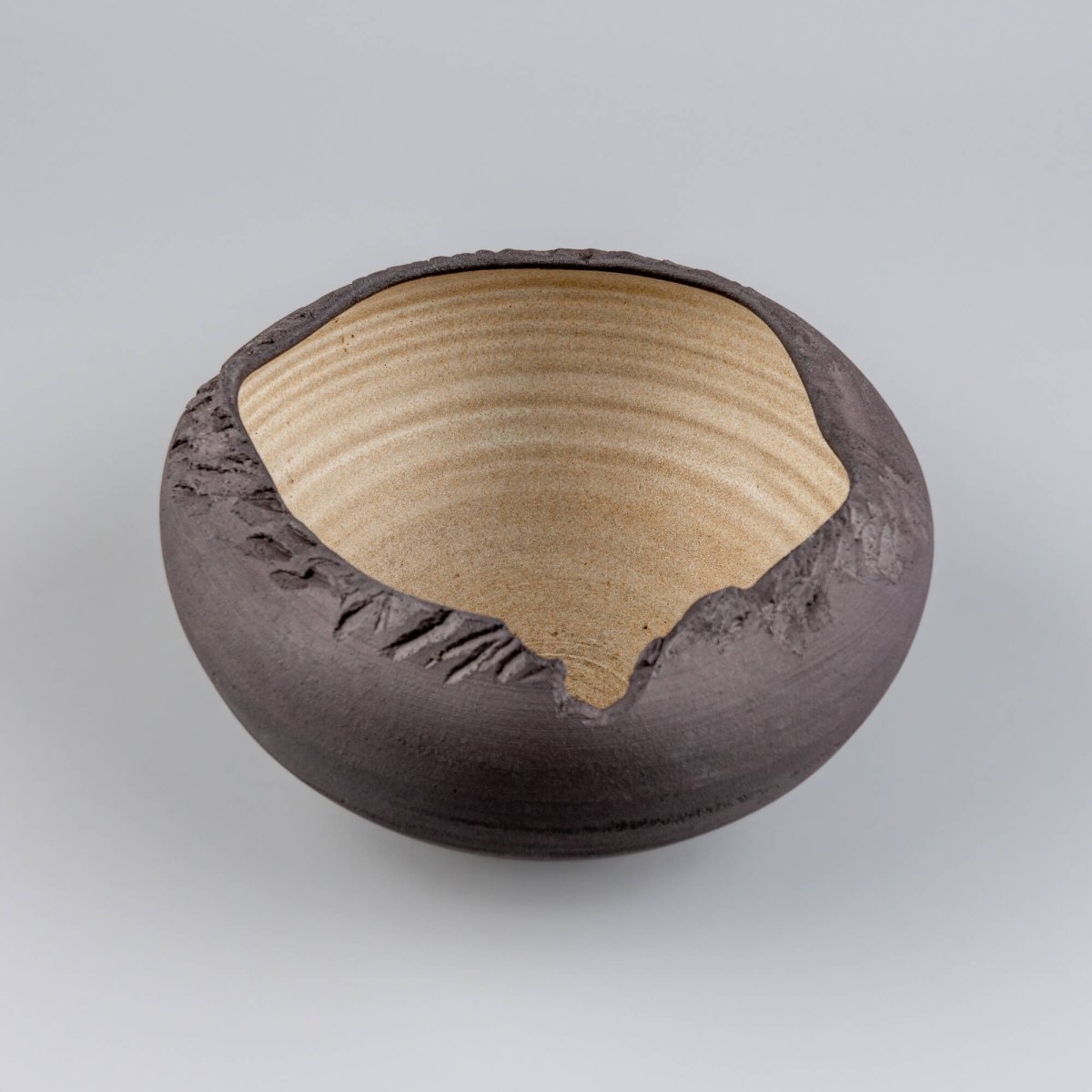 Angled front view of black stoneware bowl with natural textured surface and glazed interior.
