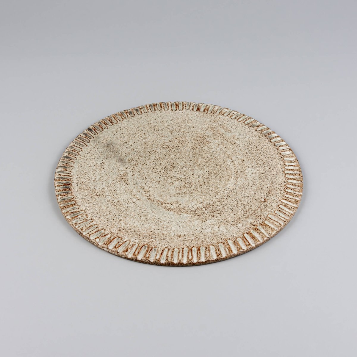 Flat handmade plate shown from side, highlighting refined stoneware form.