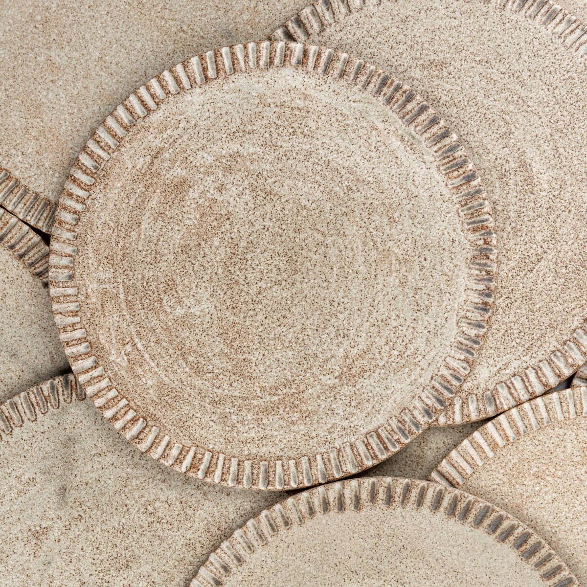 Stack of artisanal ceramic plates with matte glaze and decorative carved rims.