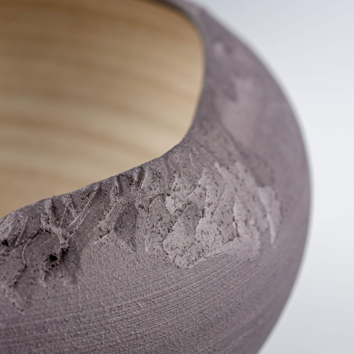Macro detail of carved edge and matte black stoneware finish on artisan bowl.