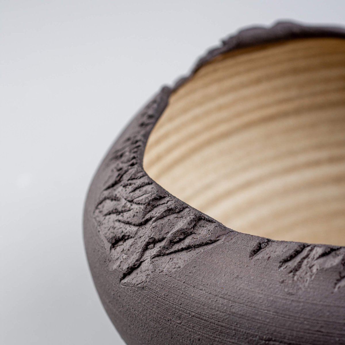 Side angle showcasing rough rim detail and dark stoneware texture on artisan-crafted bowl.
