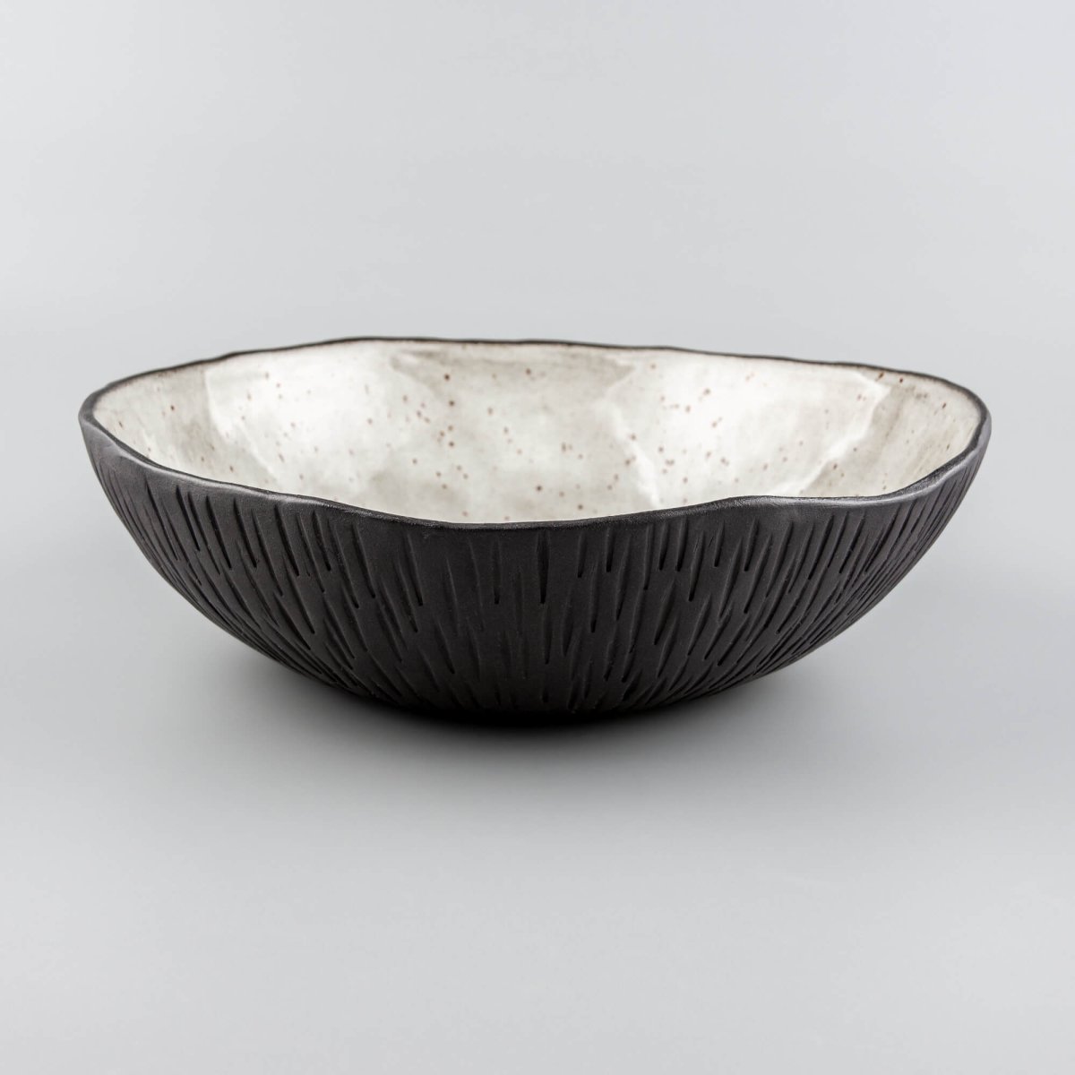 Side view of artisan ceramic bowl with black clay texture and light speckled glaze interior.