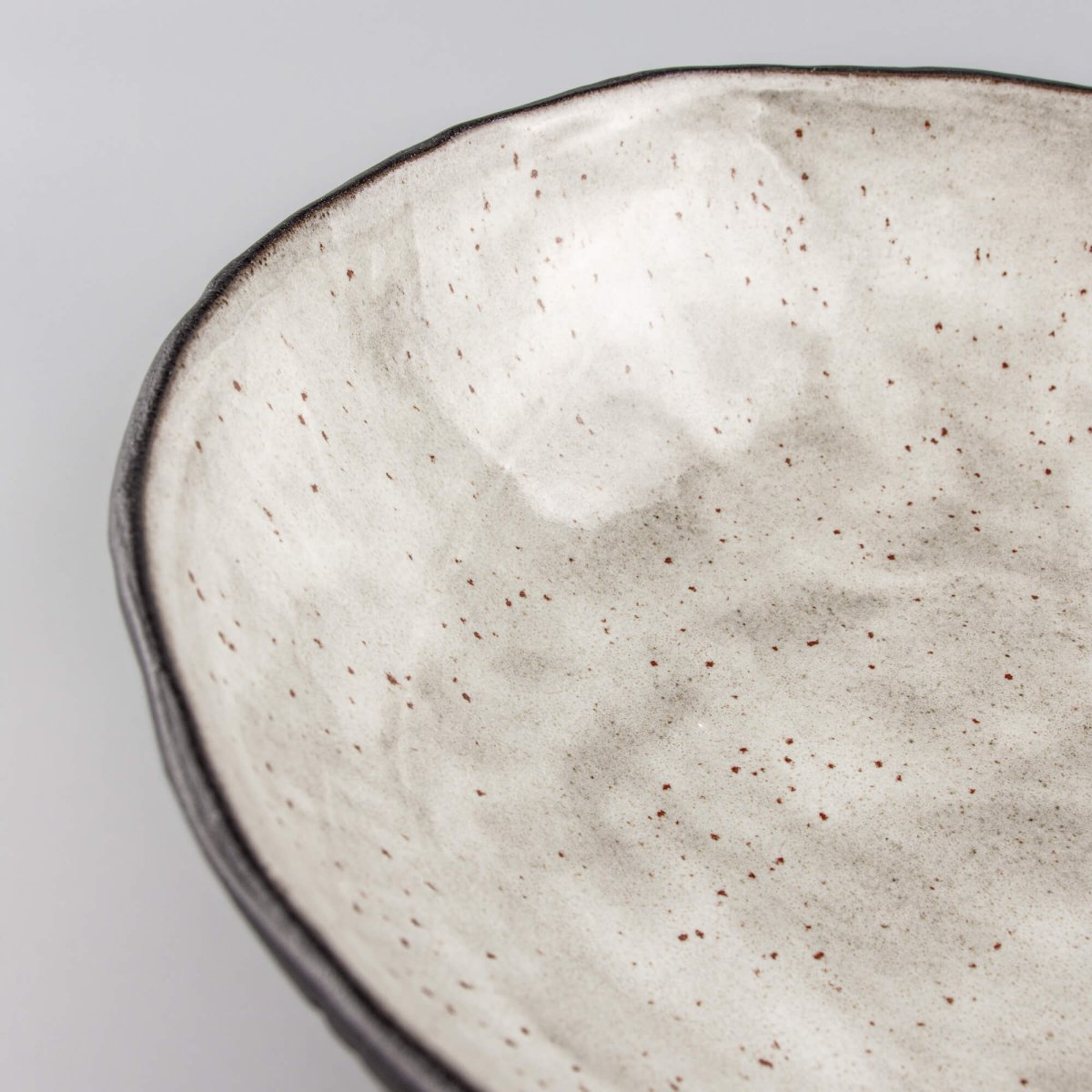 Close-up corner of ceramic bowl showing textured dark stoneware and smooth glossy inner surface.