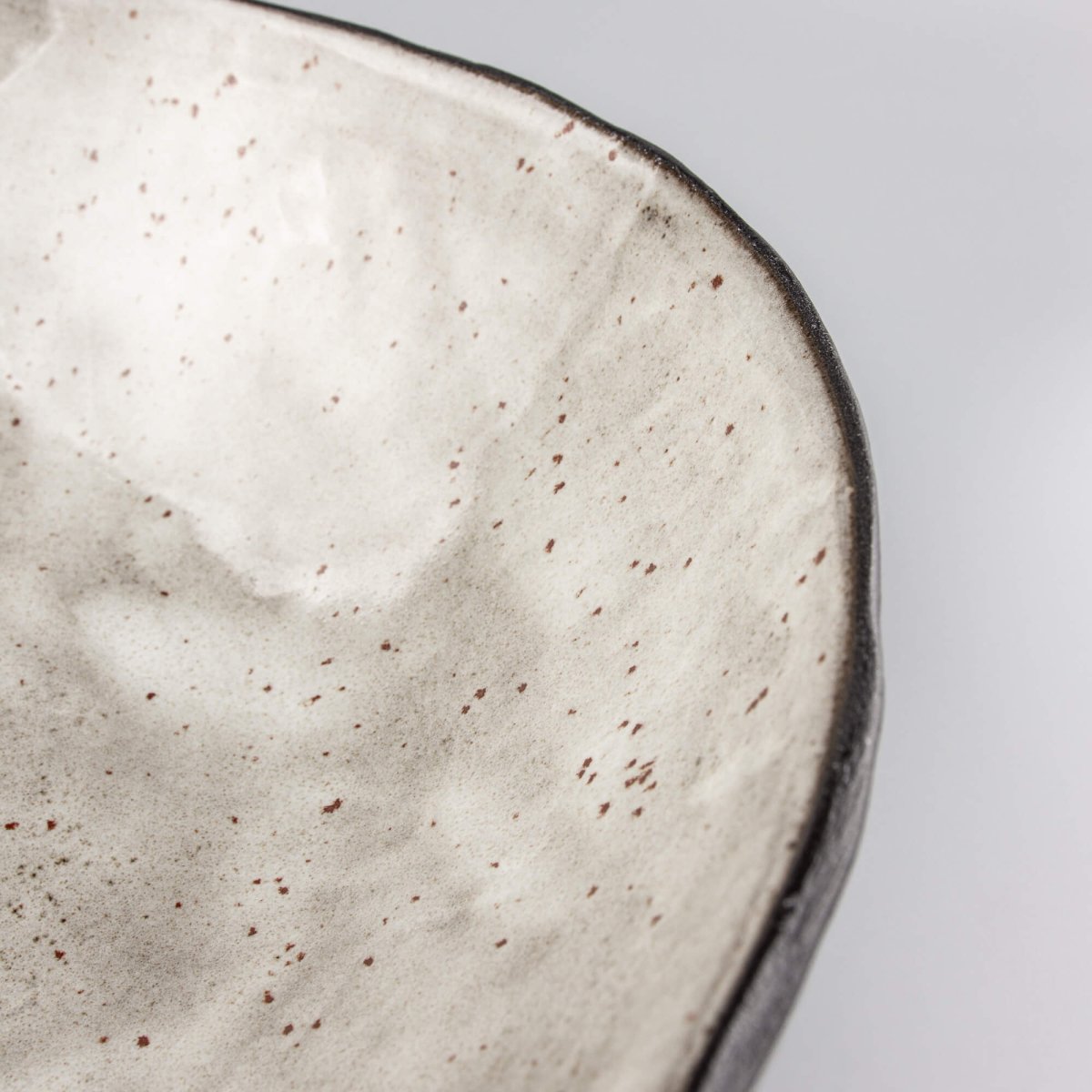 Interior detail of speckled beige glaze on handmade ceramic serving bowl with flowing form.
