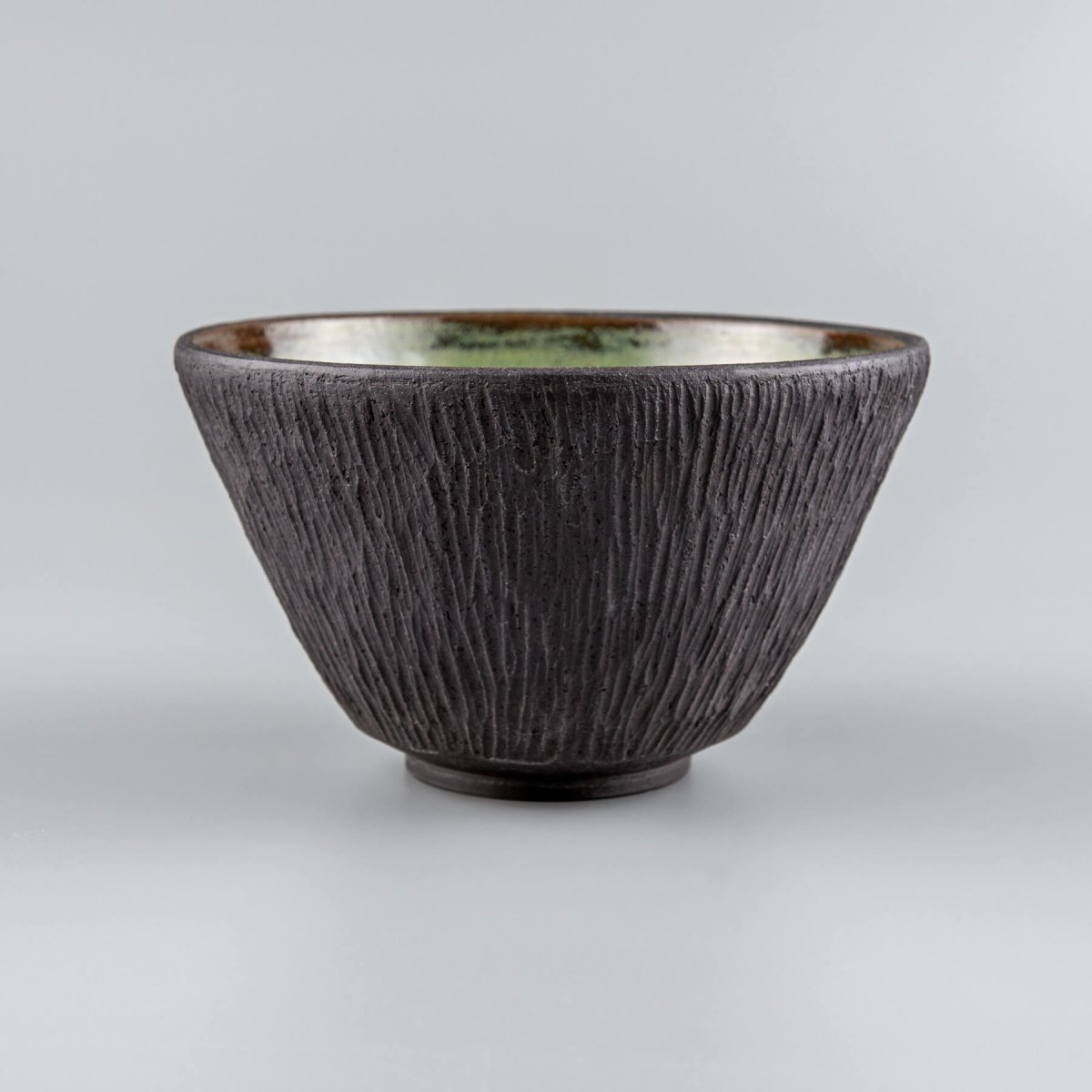 Handmade ceramic bowl with textured black clay and glossy green glazed interior for fine dining settings.