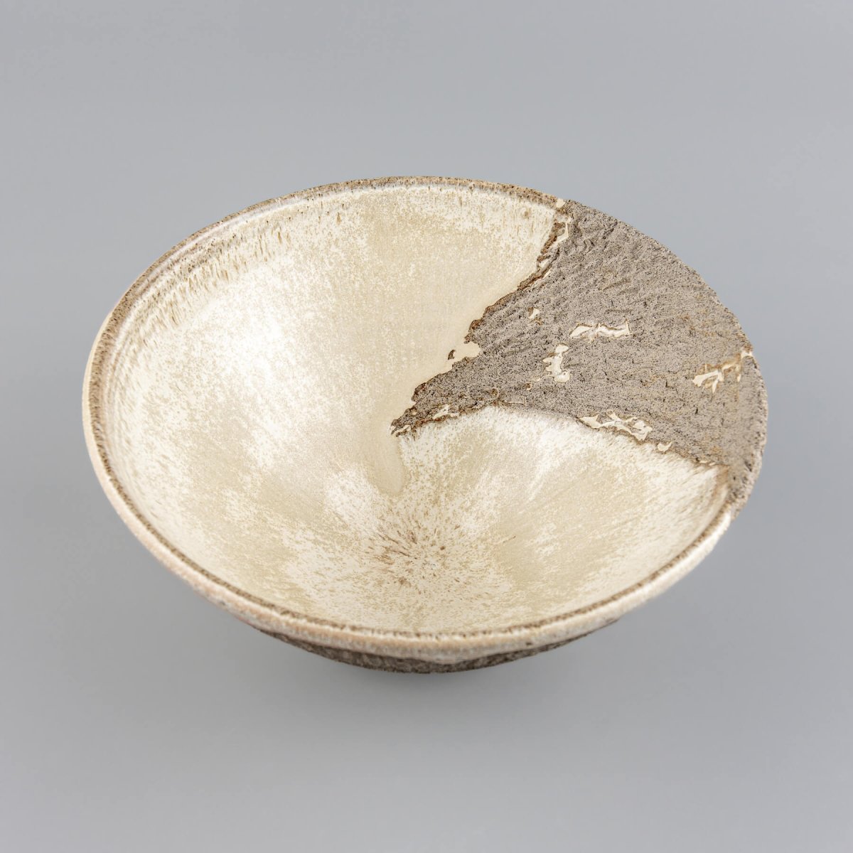 Angled handcrafted decorative bowl showcasing contrast between raw textured clay and smooth glazed surface.