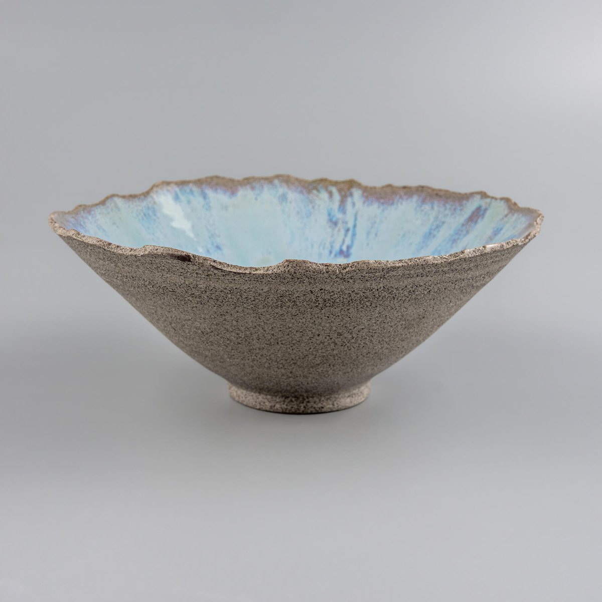 Angled view of handmade stoneware bowl with flared edges and light blue glazed interior.