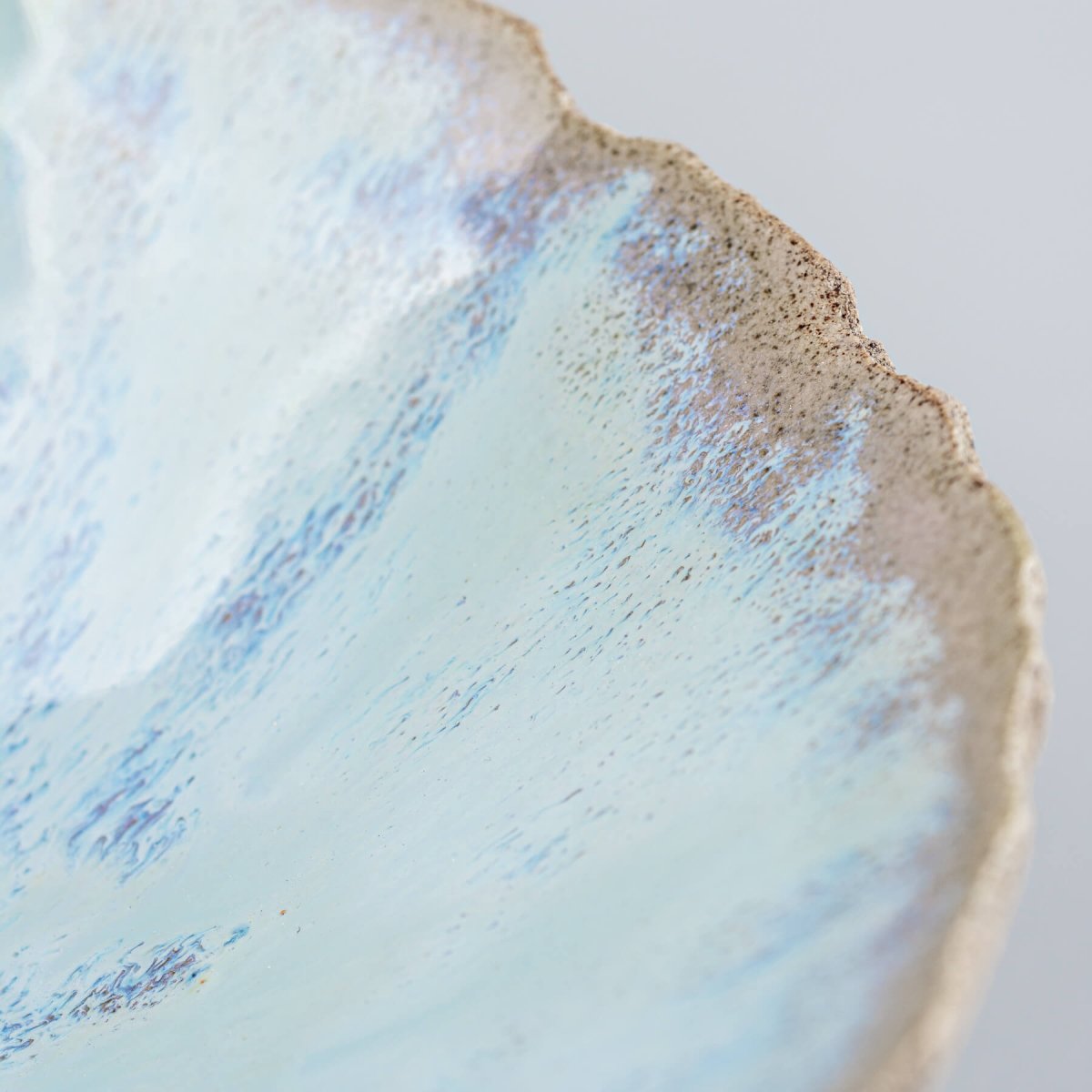 Close-up of textured rim on stoneware bowl with layered glaze in soft blue tones.