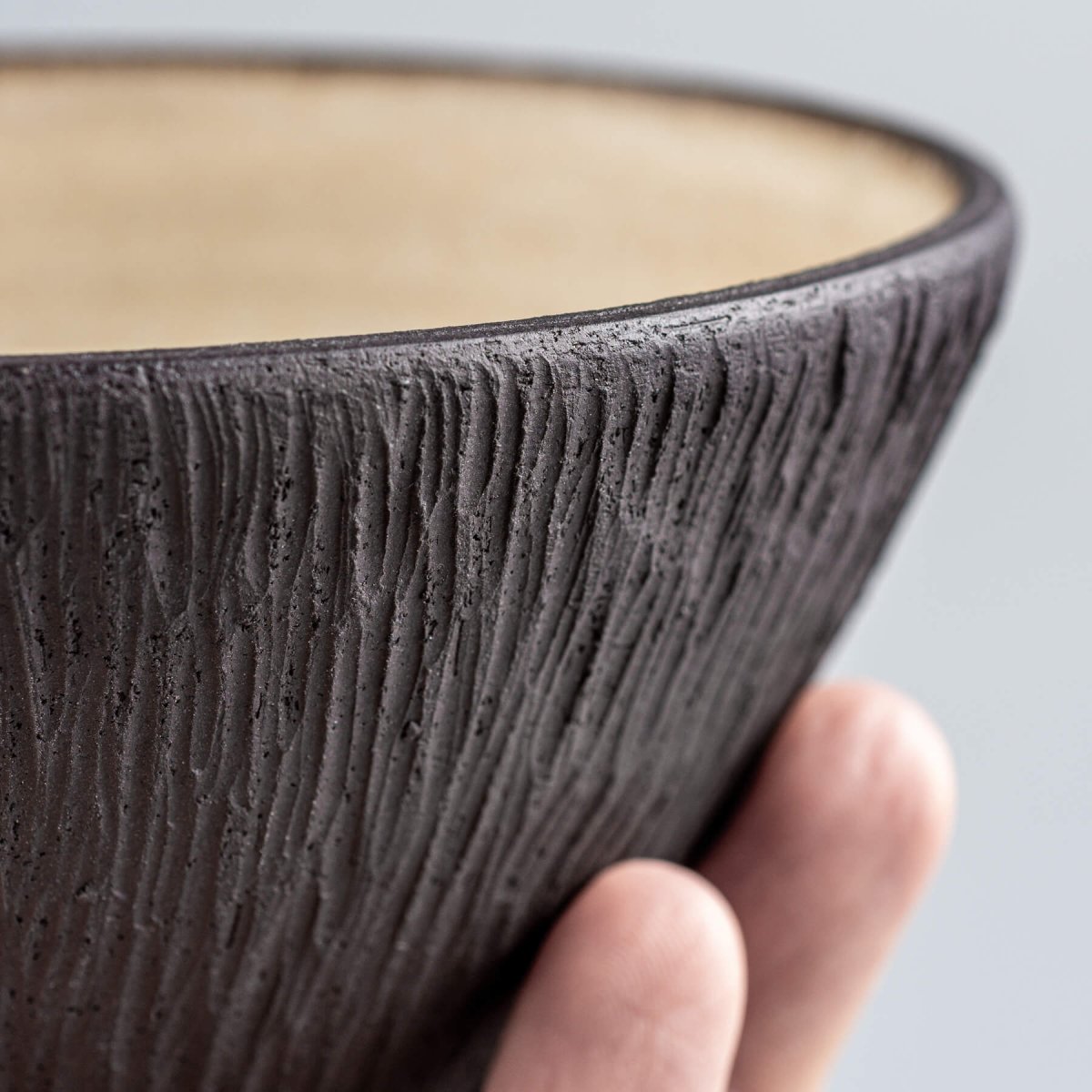 Hand holding a luxury ceramic bowl with carved exterior and beige glazed interior.
