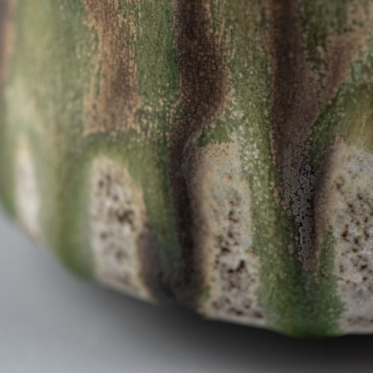 Handcrafted ceramic mug detail with layered green and brown glaze, showing fine texture and artisanal finish.