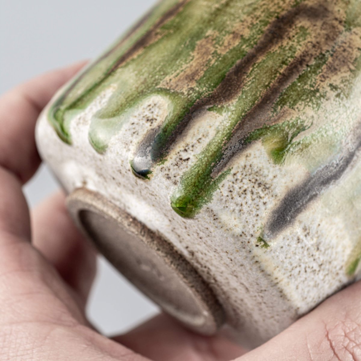 Green and brown glazed ceramic mug with handmade details and artistic finish.