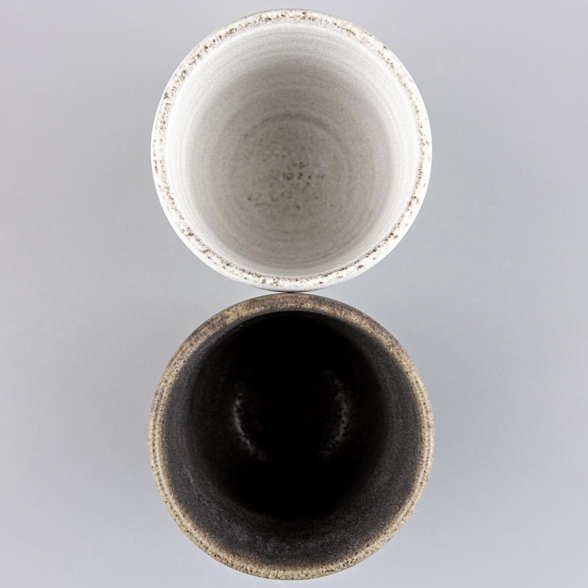 Handmade pottery cups, top view, showcasing white matte and dark olive glaze contrast for fine dining.