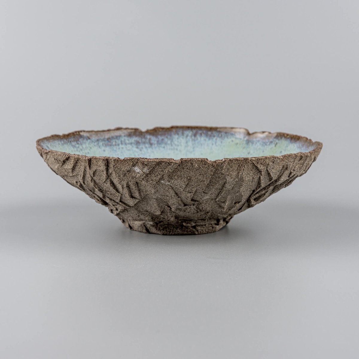 Artisan ceramic bowl with carved dark stoneware texture and glossy blue glazed interior.