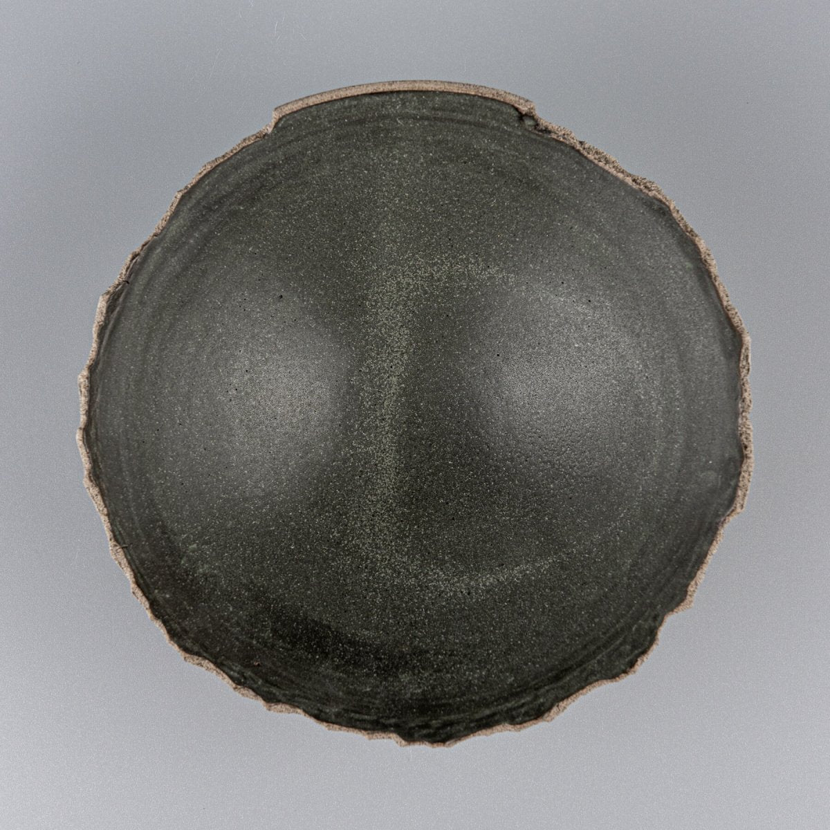 Top view of handmade pottery bowl with dark matte glaze and organic rim design, perfect for tableware.