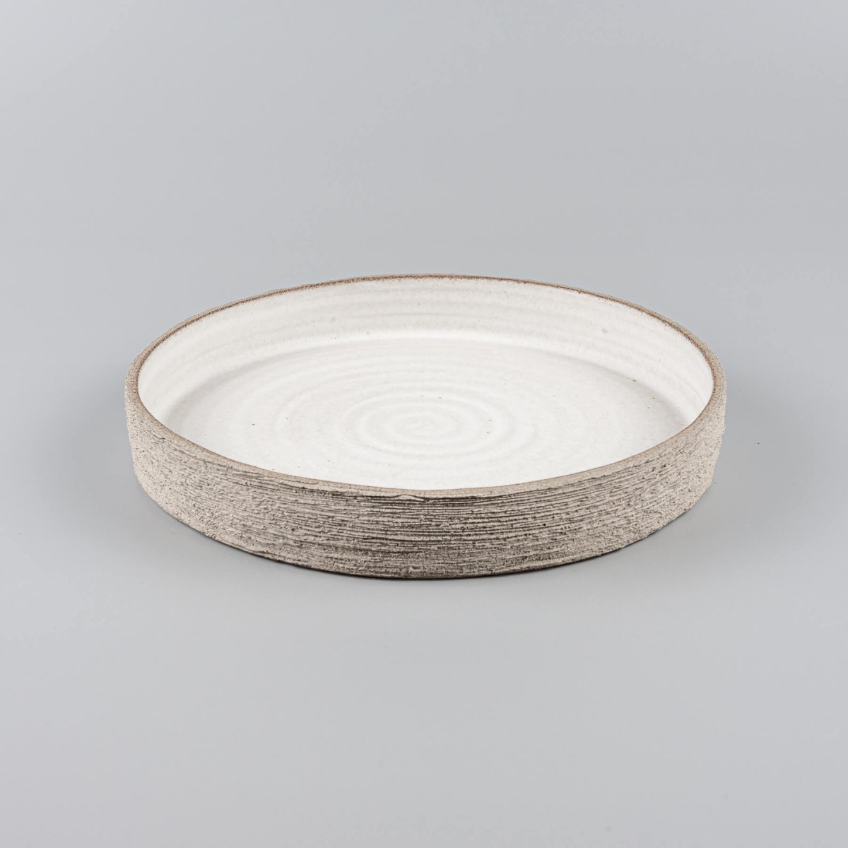 Elegant modern ceramic plate with flat base and unglazed hand-carved outer edge.