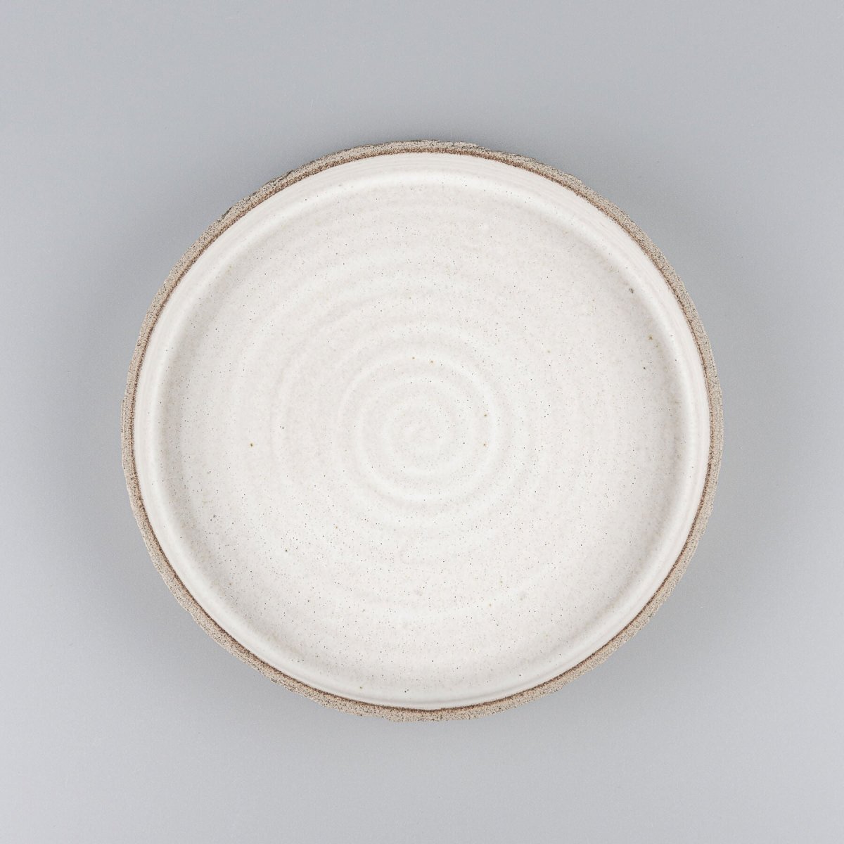 Elegant handmade ceramic plate with spiral interior and unglazed textured exterior for fine dining presentations.