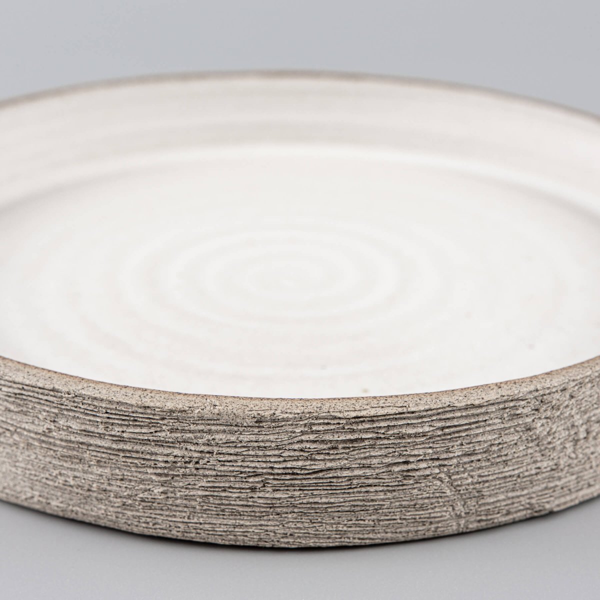Crafted stoneware plates showing textured sides and modern clean white interior.